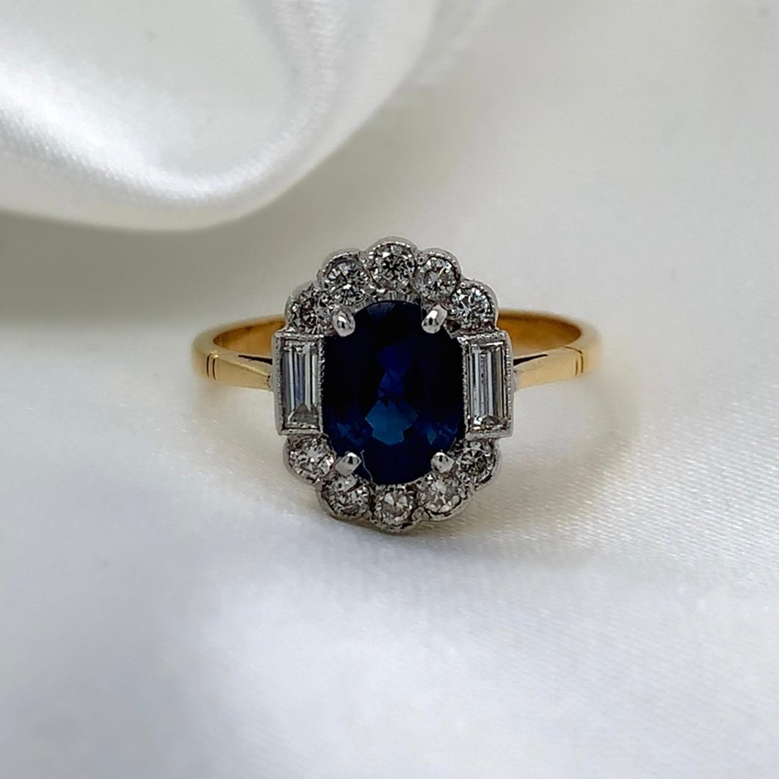 Lumi Sapphire Art Deco Ring, oval Ceylon sapphire surrounded by a diamond cluster with baguette diamond shoulders, 18ct two-tone gold, from Ebony Jewellers Chichester